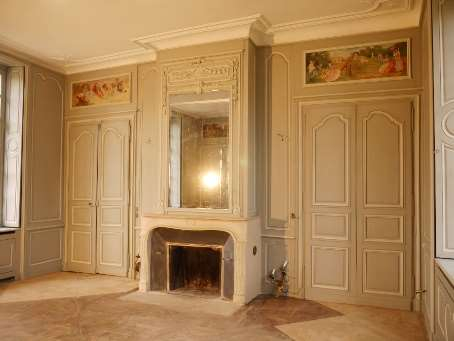 DÉCOR PEINT : Dans la salle à manger ovale d’un appartement parisien, composition de patine marmorisée sur les murs et pastillée sur les portes, avec imitation pierre sur les pilastres. La cuisine attenante est en patine vert foncé.