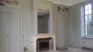 DECOR PEINT : Dans un salon d'un château classé monument historique français, décor peint des boiseries du XVIIIe siècle dans un style classique -détail des patines de 2 tons, gris et blanc cassé, avec restauration de l'aspect de la cheminée et des 4 peintures en dessus de porte