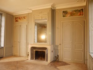 DECOR PEINT : Dans un salon d'un château classé monument historique français, décor peint des boiseries du XVIIIe siècle dans un style classique -détail des patines de 2 tons, gris et blanc cassé, avec restauration de l'aspect de la cheminée et des 4 peintures en dessus de porte