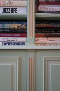 DECOR PEINT : dans un appartement parisien, filets dorés et clairs sur les moulures d’une bibliothèque verte. Détail.