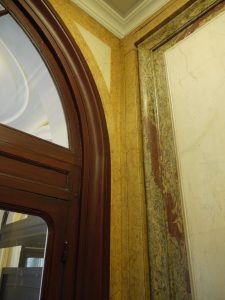 RESTAURATION : restitution des stucs marbres suite à la rénovation des gaines électriques et restauration de l’imitation acajou sur la porte d’entrée (détail)