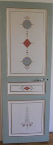 TROMPE L'OEIL : Sur la porte de la chambre d'un appartement parisien, décor de style Directoire, composé de patines de tons blanc cassé et bleu pâle, avec ornements en arabesque et filets dorés.