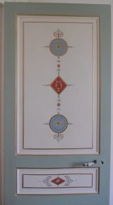 TROMPE L'OEIL : Sur la porte de la chambre d'un appartement parisien, décor de style Directoire, composé de patines de tons blanc cassé et bleu pâle, avec ornements en arabesque et filets dorés.