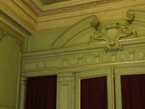 DECOR PEINT : Dans un petit salon d’un appartement parisien, réalisation d’un décor néoclassique de patines de ton vert sur les murs et de ton beige sur la corniche, avec filets de dorure sur les moulures ornementées. (Détail du portique)