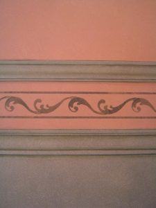 DÉCOR PEINT : Dans le salon d'un mas provençal, décor de facture modeste, en composition de 2 tons de patines; soubassement en patine gris vert, avec fausses moulures et motif de frise. Détail