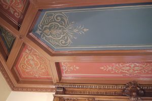 RESTAURATION : Dans les caissons au plafond d'une salle à manger de style néogothique, restauration des décors de motifs et filets taupe et dorés, sur fonds verts ou rouges. Détail.