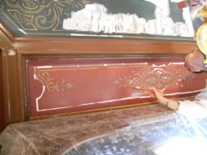 RESTAURATION : Dans les caissons au plafond d'une salle à manger de style néogothique, restauration des décors de motifs et filets taupe et dorés, sur fonds verts ou rouges. Détail du plafond pendant restauration.