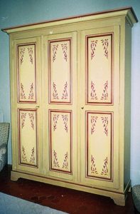 MEUBLE PEINT : Sur l'armoire de chambre d'ami d'un mas provençal, composition de motifs au pochoir cernés de filets ocres sur patines de tons blond et lin.