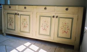 DECOR PEINT : Sur une desserte dans un mas provençal, décor de patines blondes, filets verts et motifs floral sur les portes.