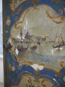 Restauration en cours du décor peint d'une petite armoire de chevet, un meuble peint de style baroque vénitien.
