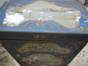 Restauration en cours du décor peint d'une petite armoire de chevet, un meuble peint de style baroque vénitien.