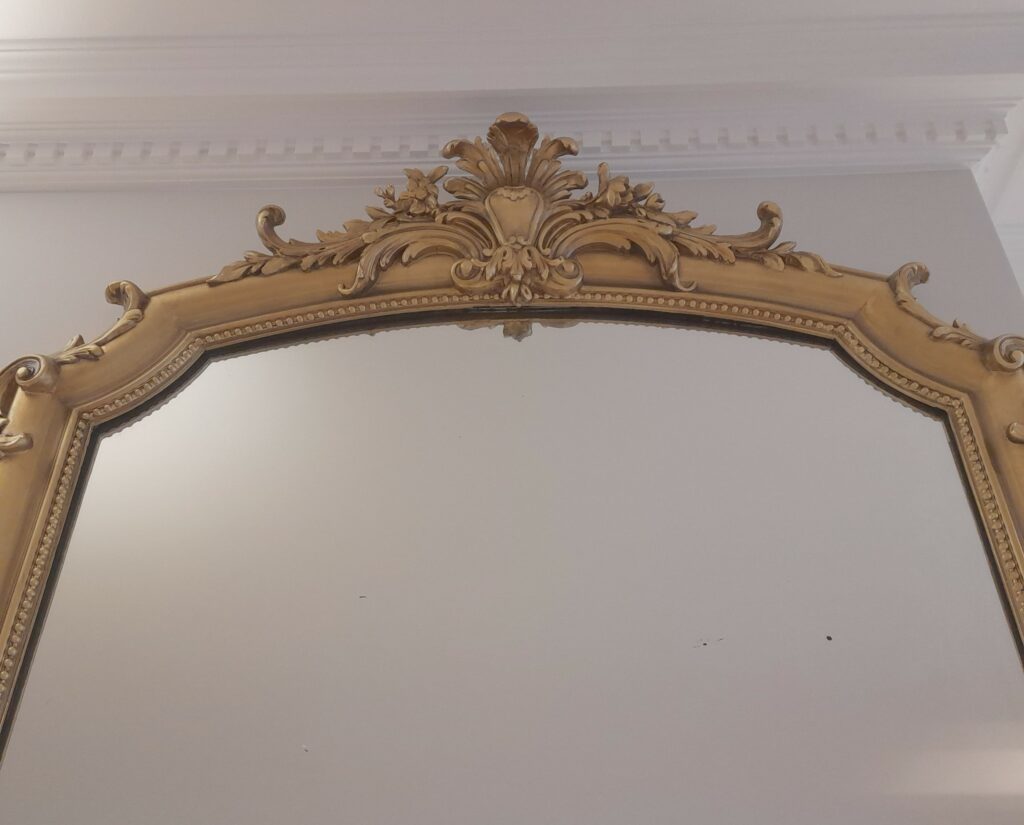 Dans un appartement contemporain, décor de trumeau, cadre de miroir doré et patiné pour un contraste d'aspect baroque élégant.